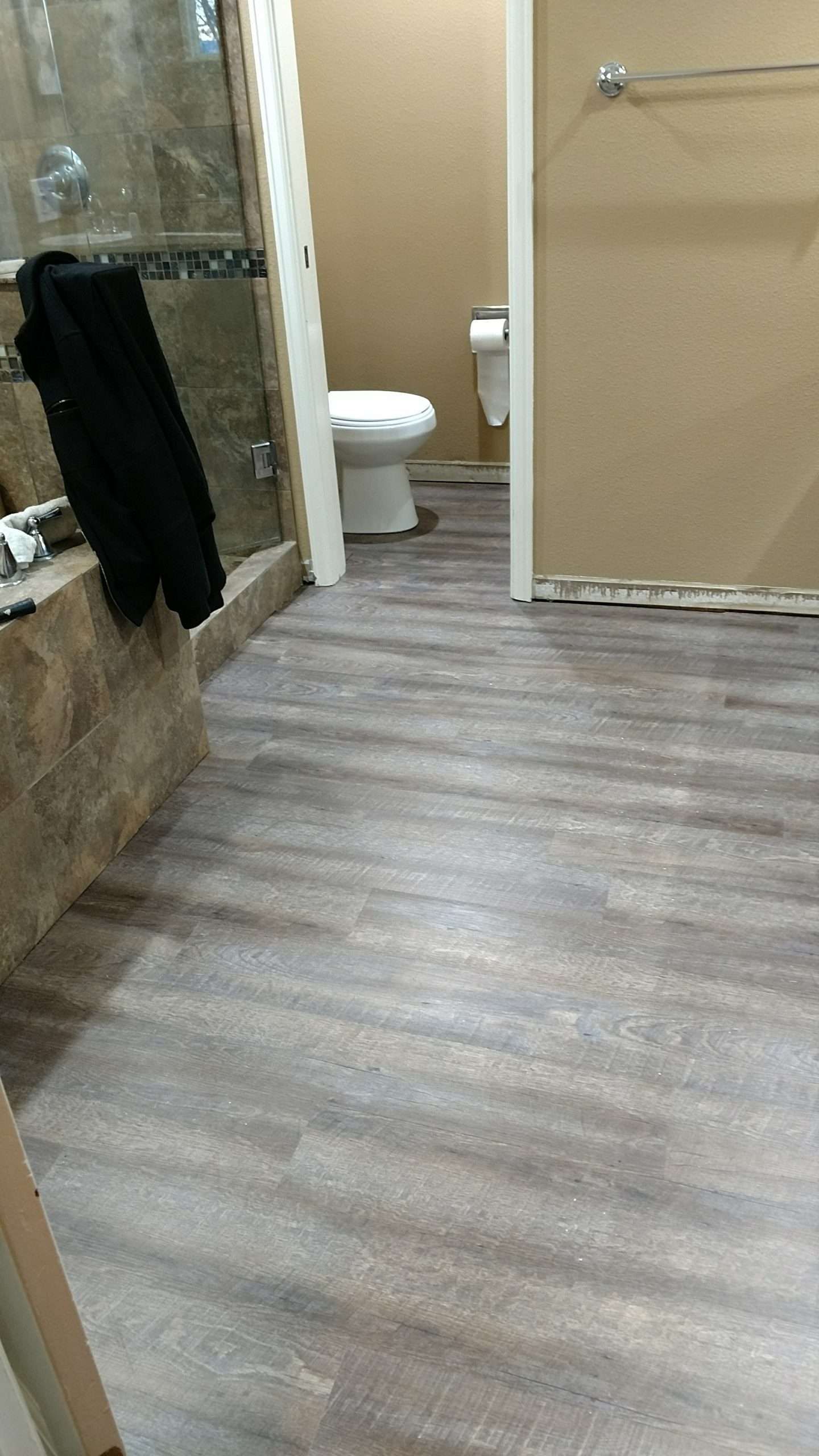 Bathroom with gray wood-look flooring, a white toilet in the doorway, and a tiled shower.