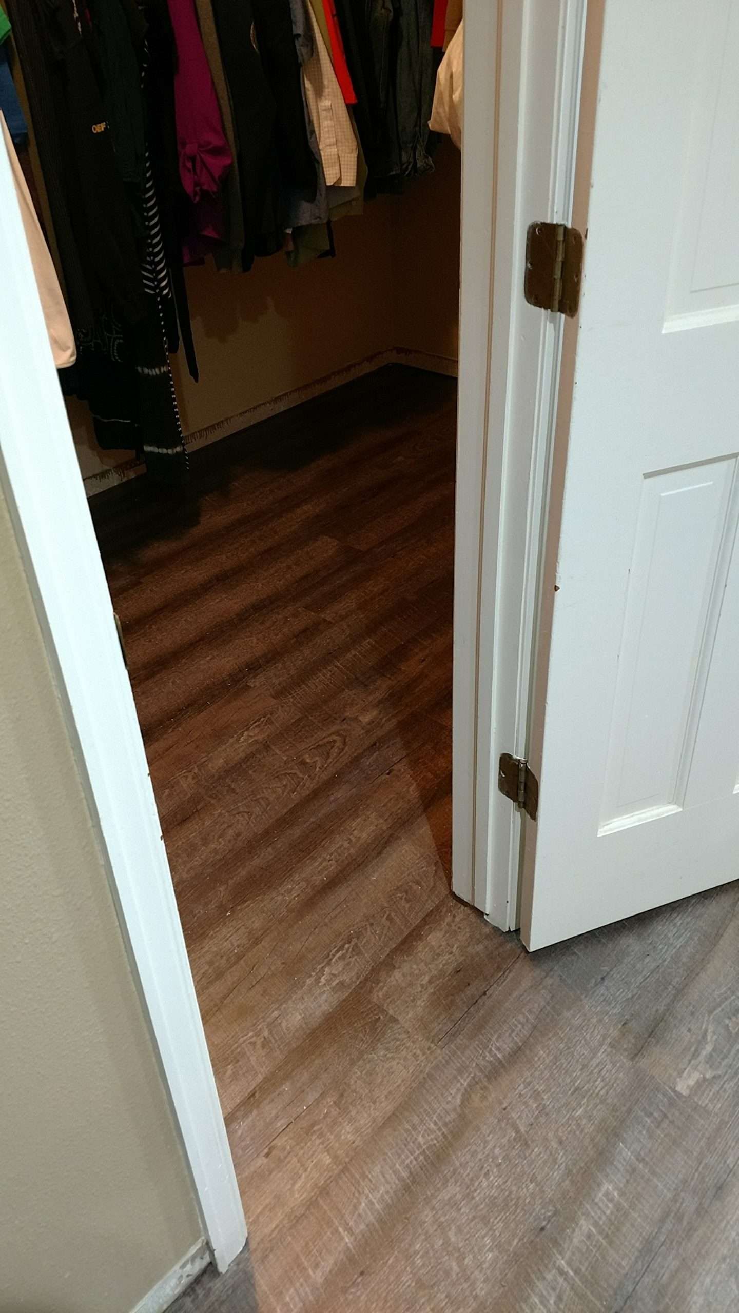 Closet doorway open, revealing clothes hanging inside; light brown floor contrasts with the dark closet.