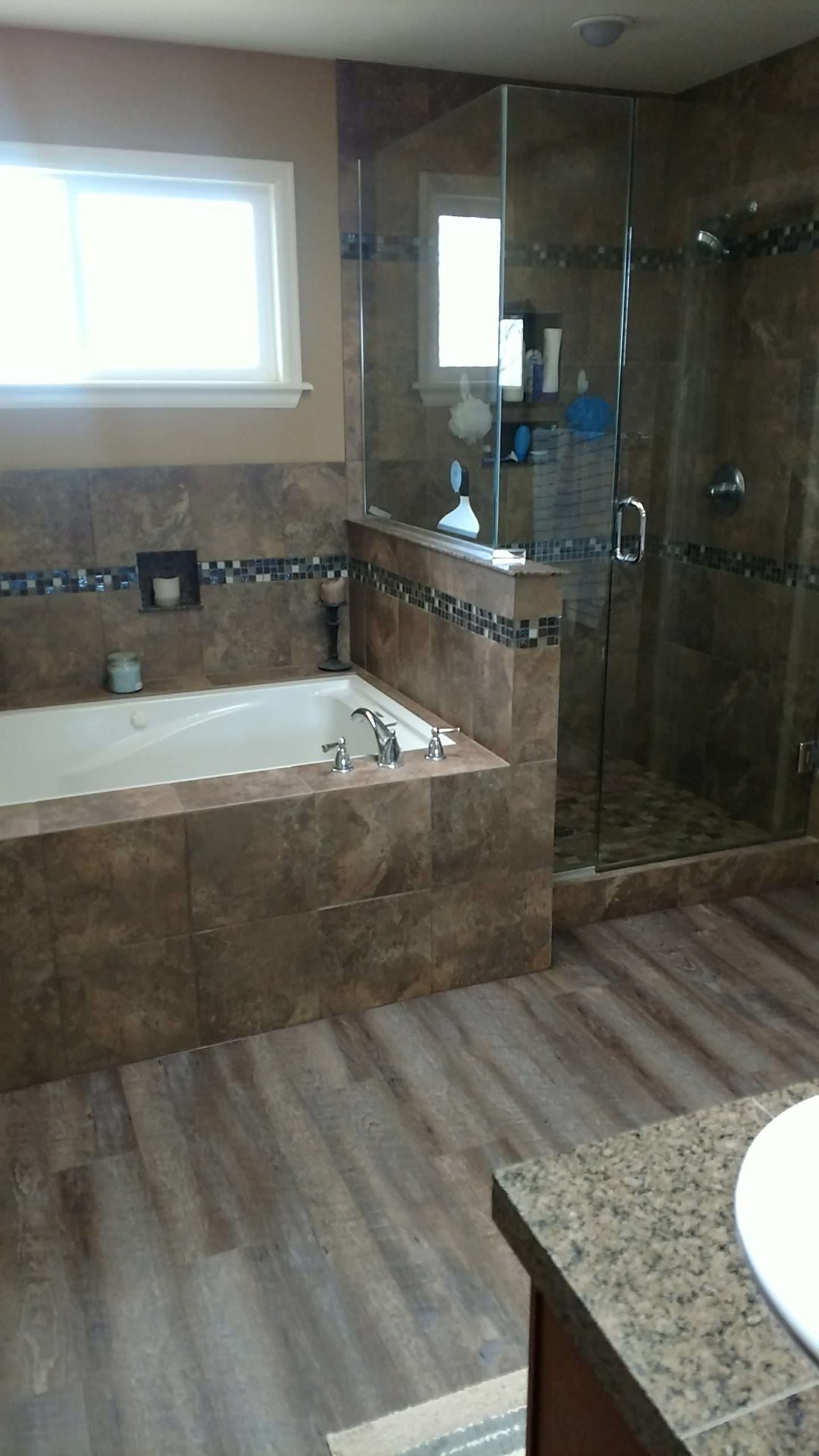 Bathroom with tub, shower, and wood-look flooring; brown tile and glass shower enclosure.