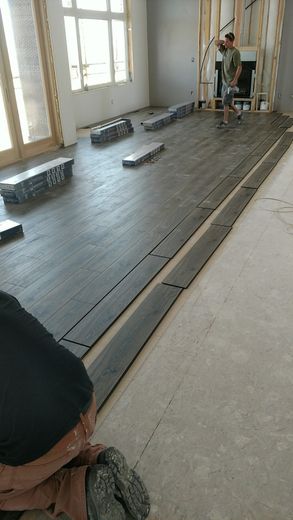 People installing dark gray floorboards in a room with windows, natural light.