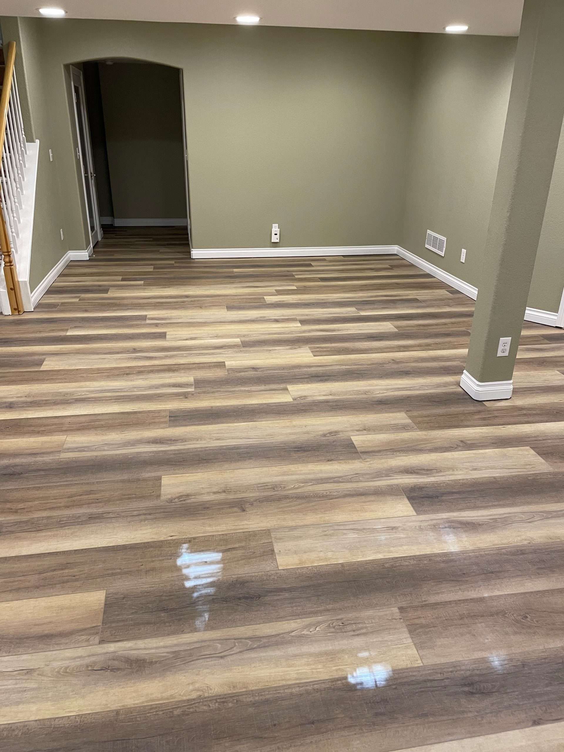 Newly installed wood-look flooring in a room with olive green walls, white trim, and a recessed doorway.
