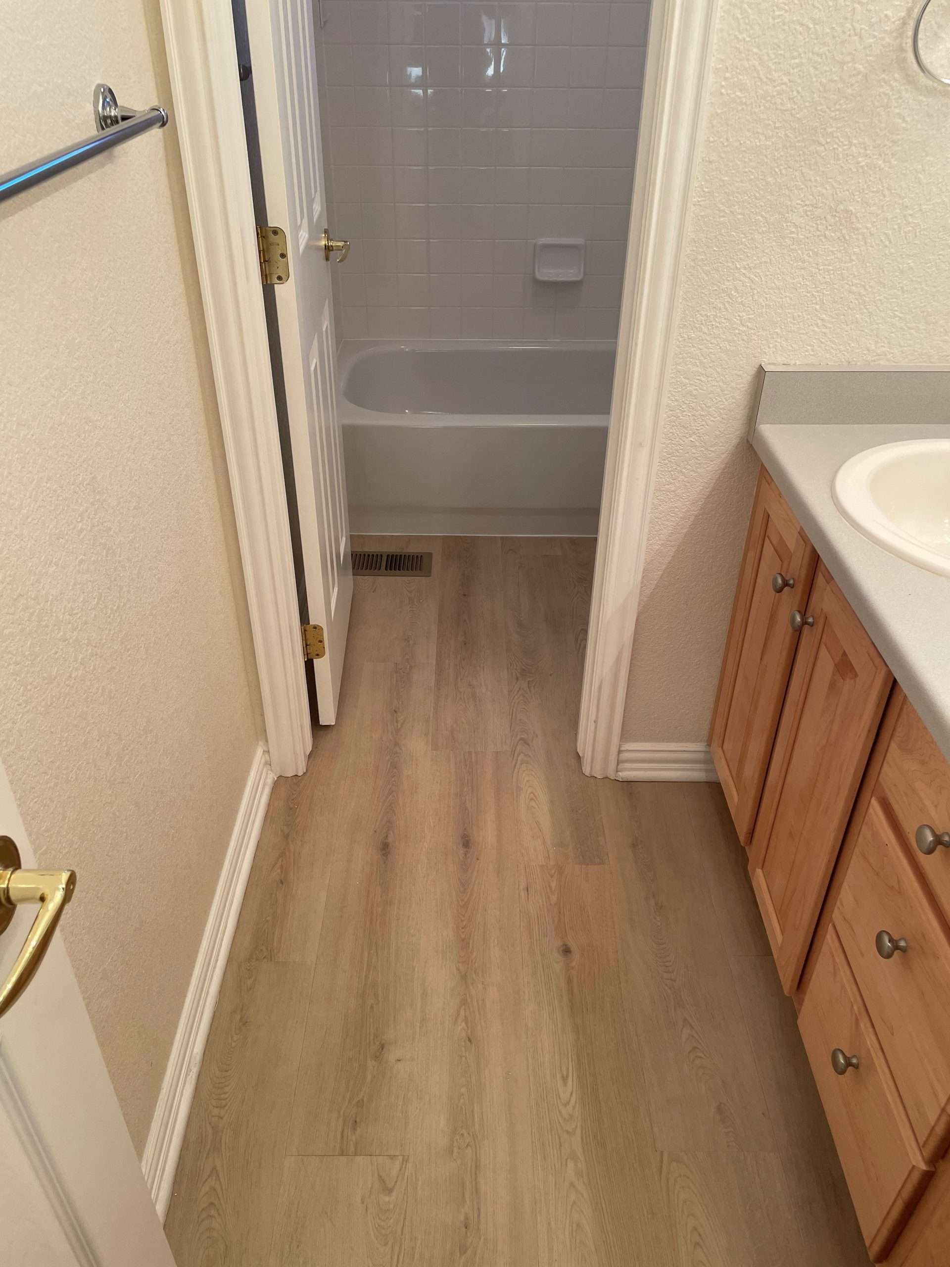 Bathroom with light wood-look flooring, a bathtub, wooden vanity, and a doorway.