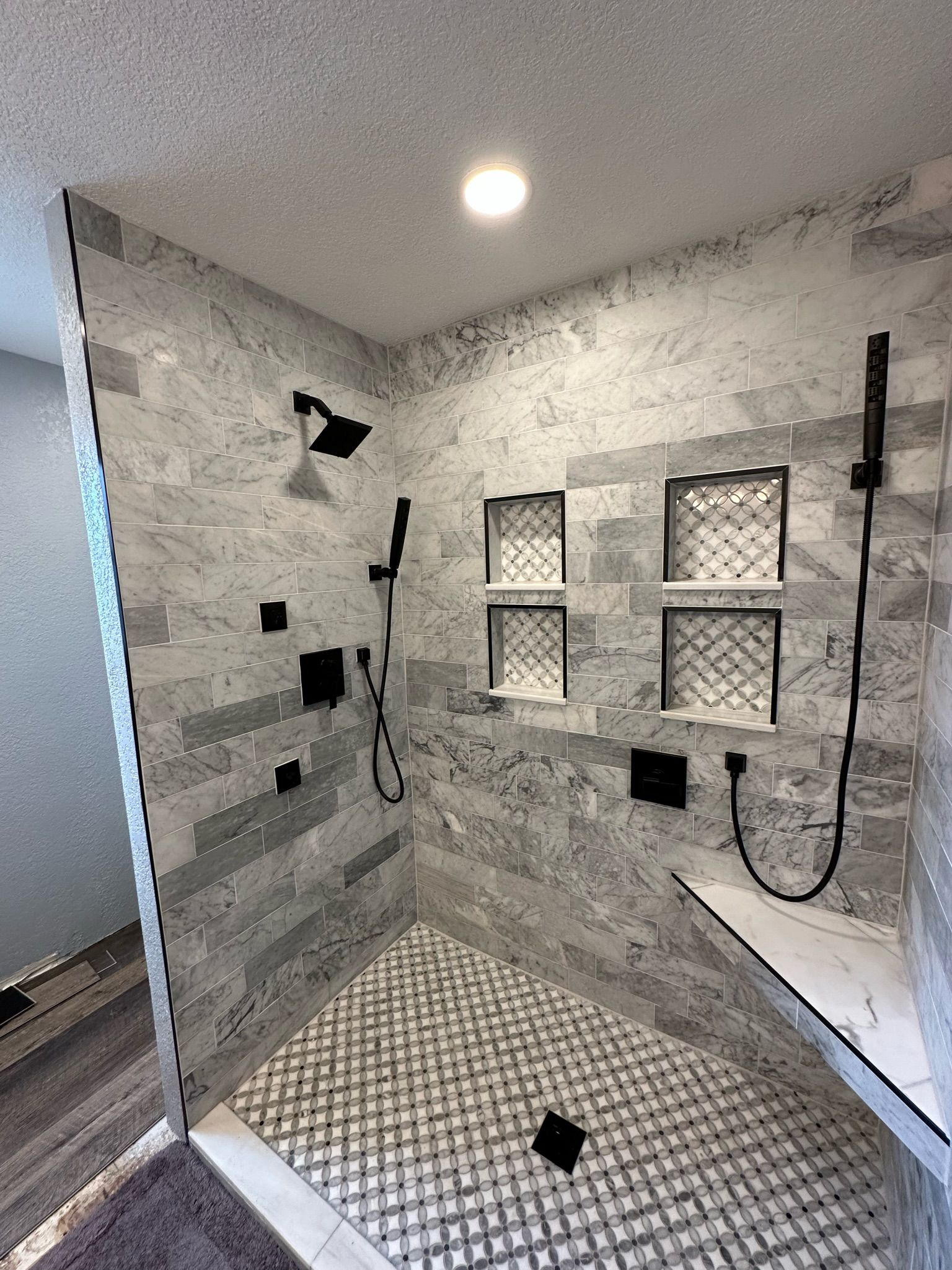 Gray tiled shower with black fixtures, built-in shelves, and glass door.