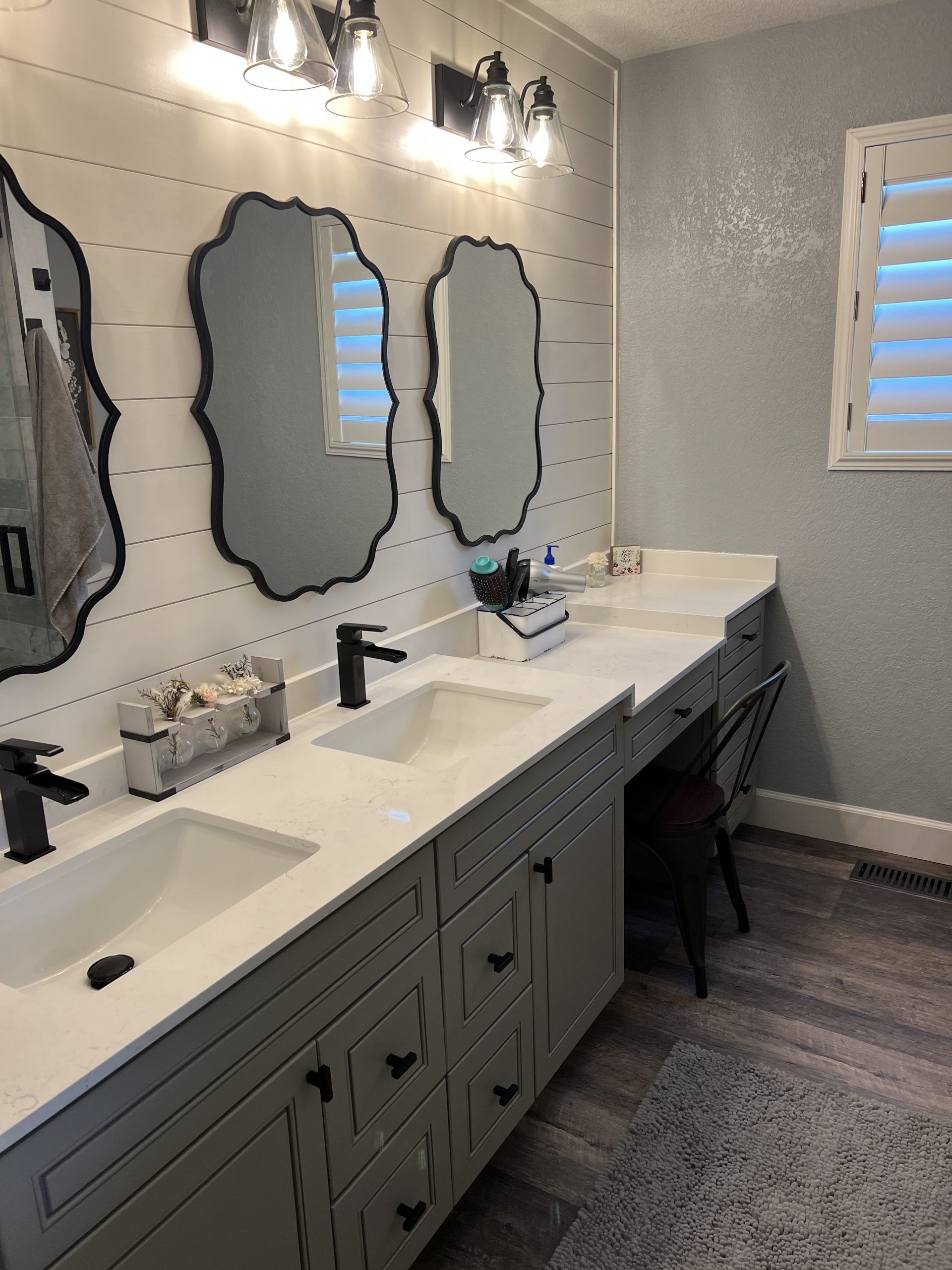 Bathroom with gray vanity, white countertop, black faucets, ornate mirrors, and shiplap accent wall.