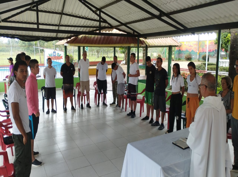 Grupo de personas vestidas con ropa informal alrededor de un sacerdote, en terapia de grupo