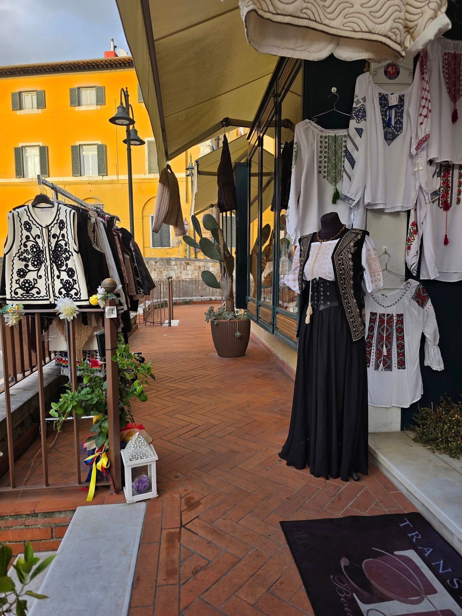 Negozio di abbigliamento sul ciglio della strada con top e abiti ricamati in bianco e nero. Edificio giallo sullo sfondo.