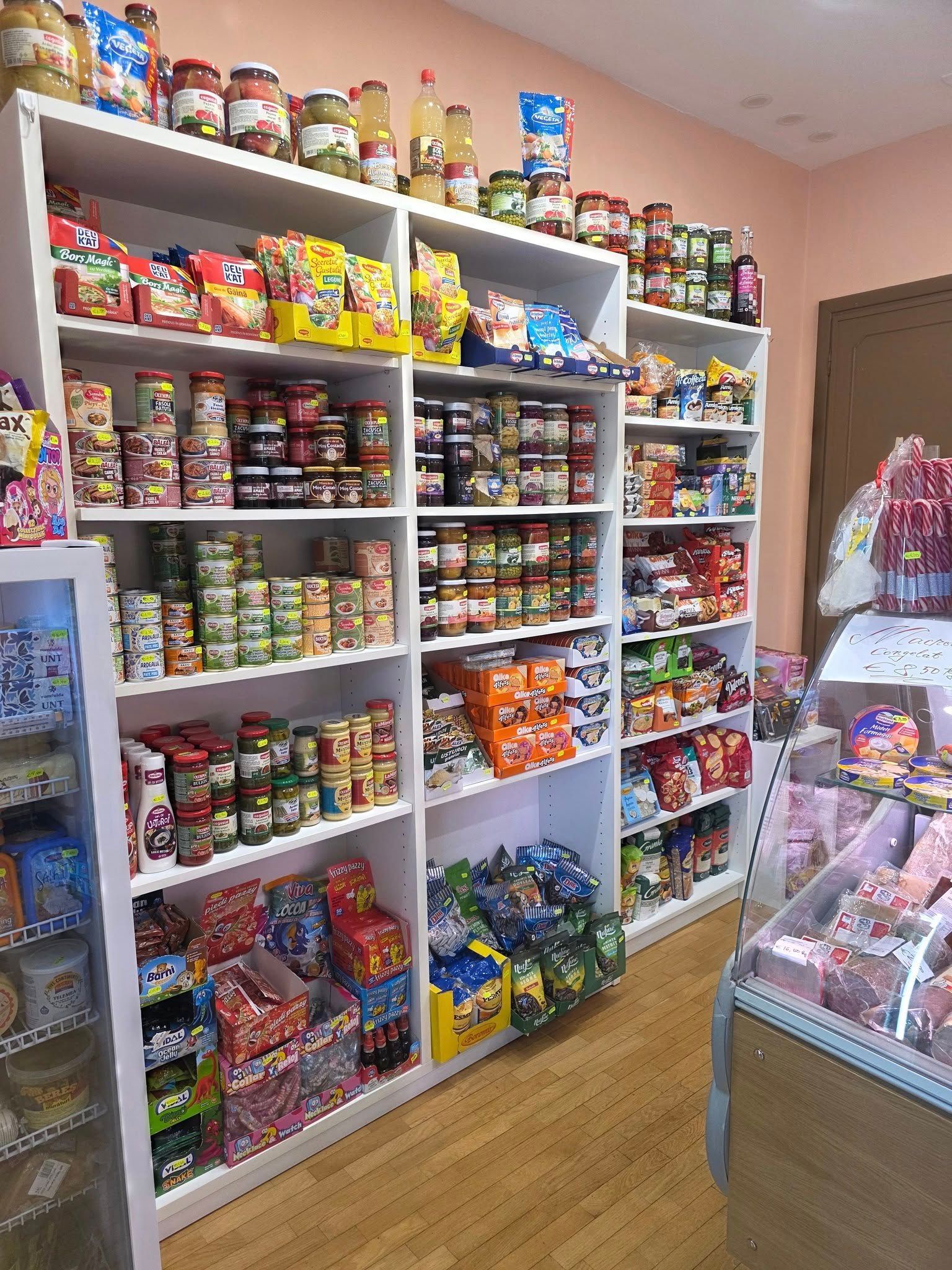 Scaffali di un negozio pieni di prodotti in scatola, barattoli e snack confezionati; pavimento in legno.