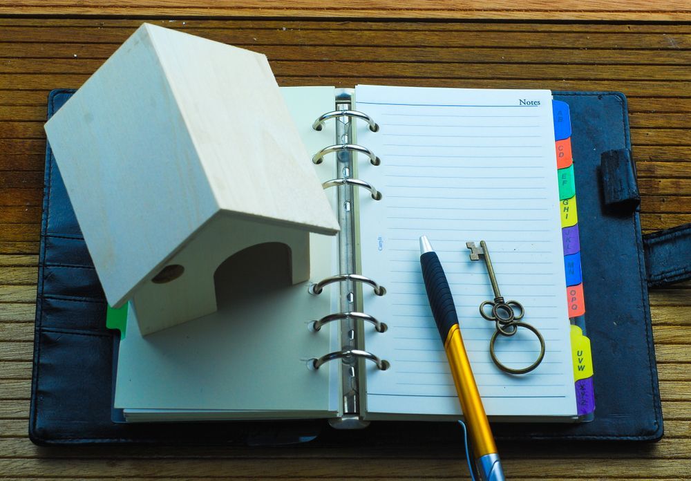A Small House Is Sitting on Top of An Open Notebook Next to A Pen and Keys - Conveyancers in Kiama, NSW