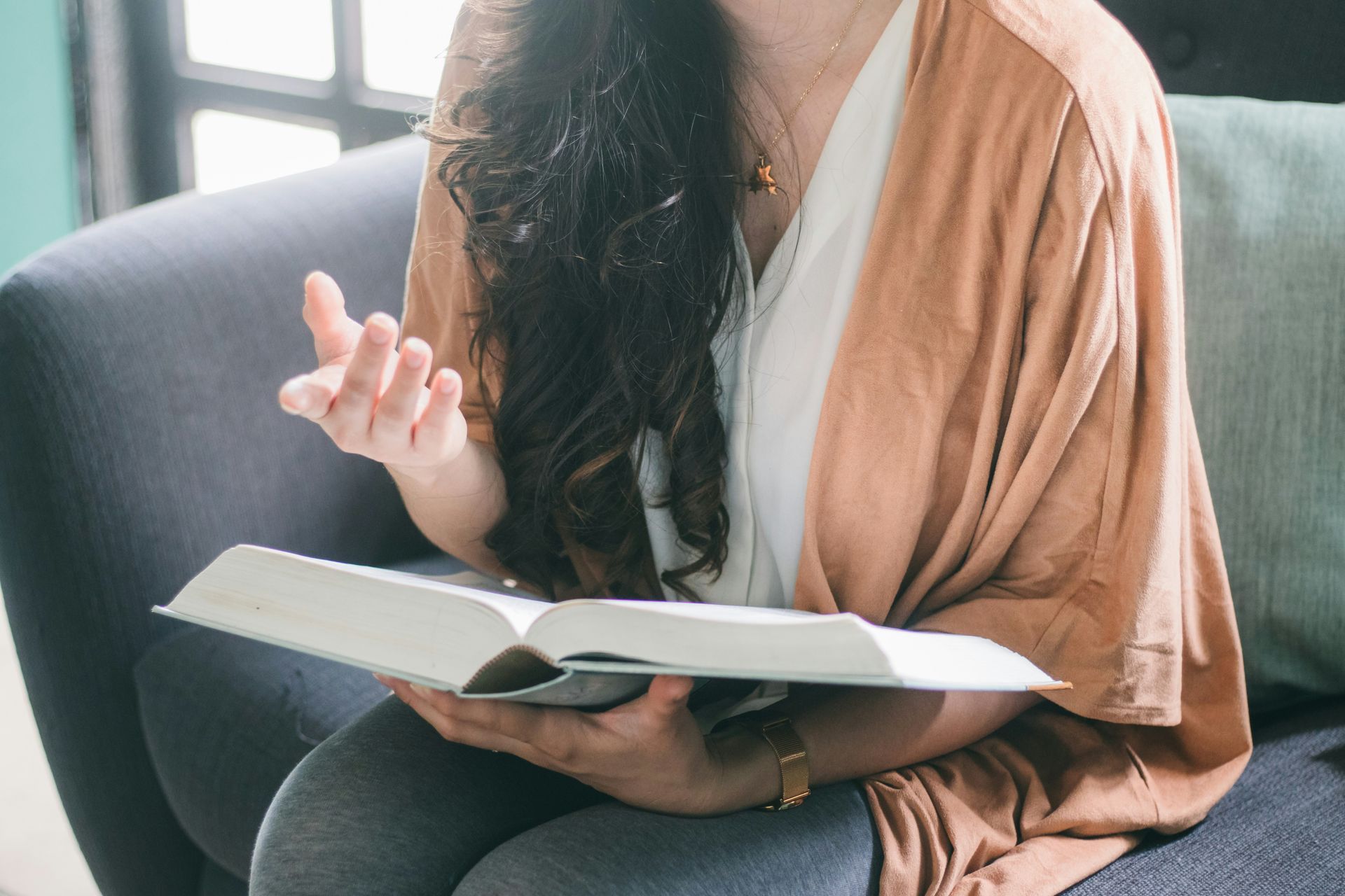 Woman seated, holding open book, gesturing with hand, soft lighting.