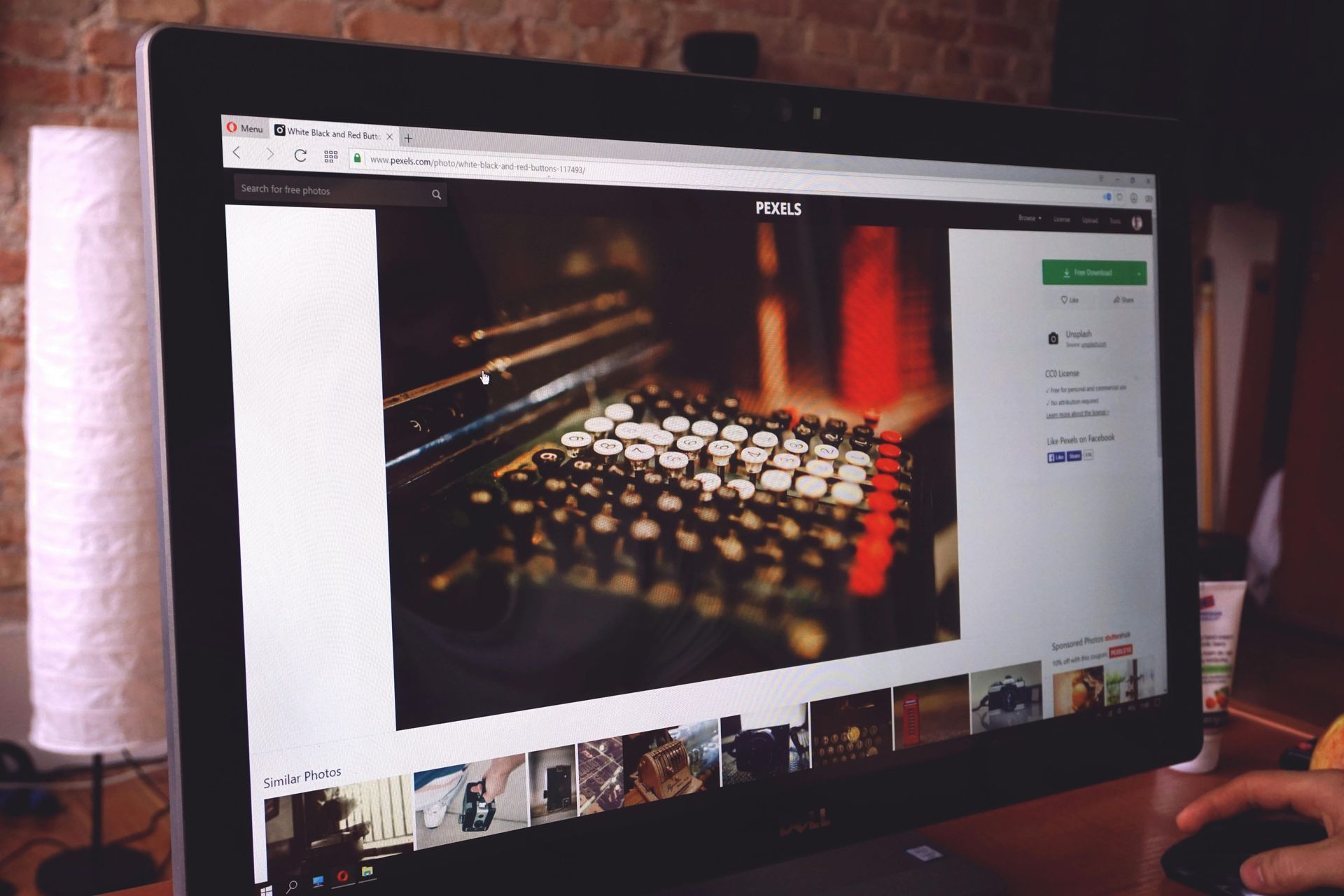 Computer monitor displays a photo of a sound mixing console. The scene has dim lighting; a person's hand is visible.