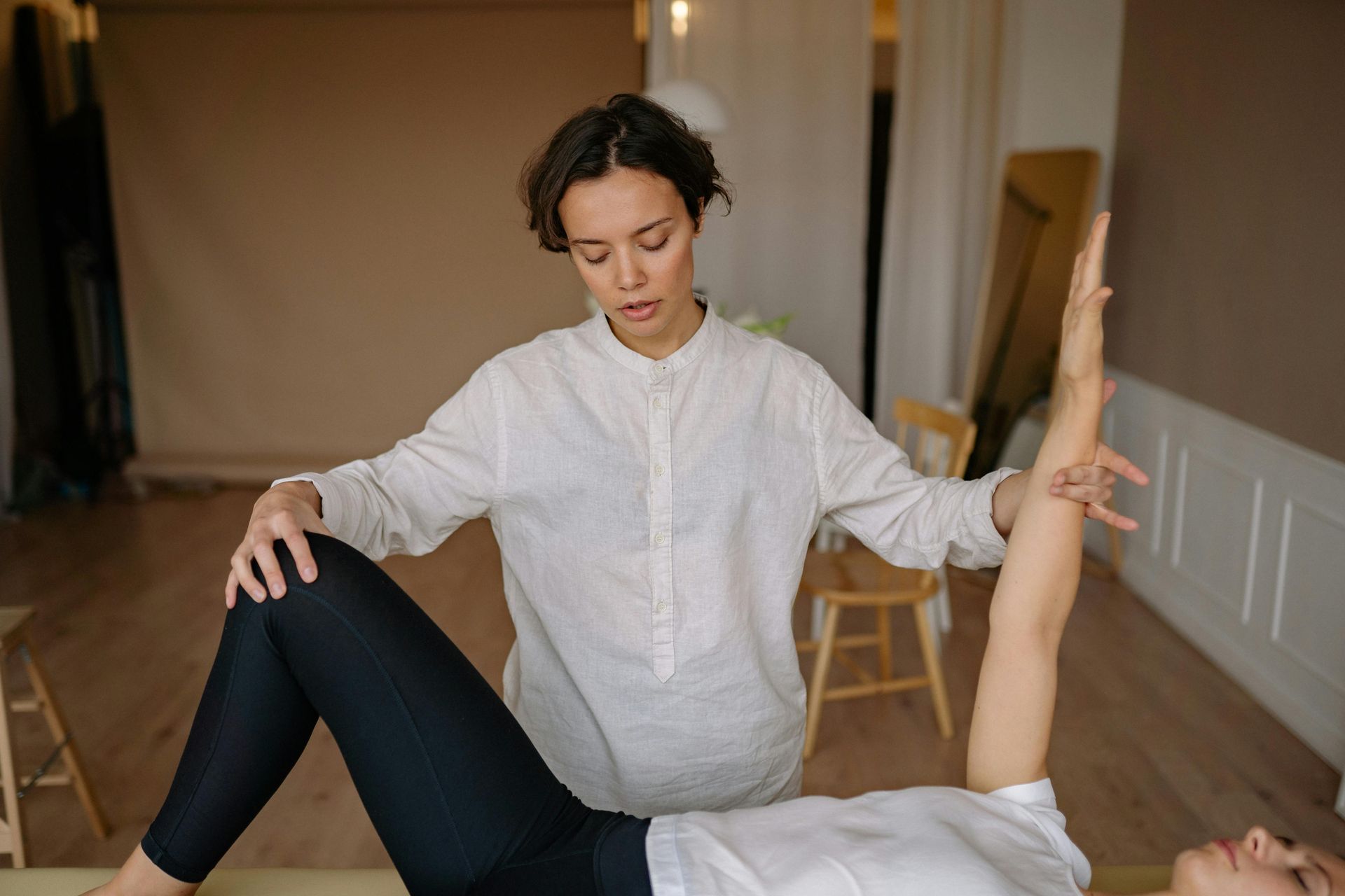 Woman assisting another woman with arm exercise, indoors.