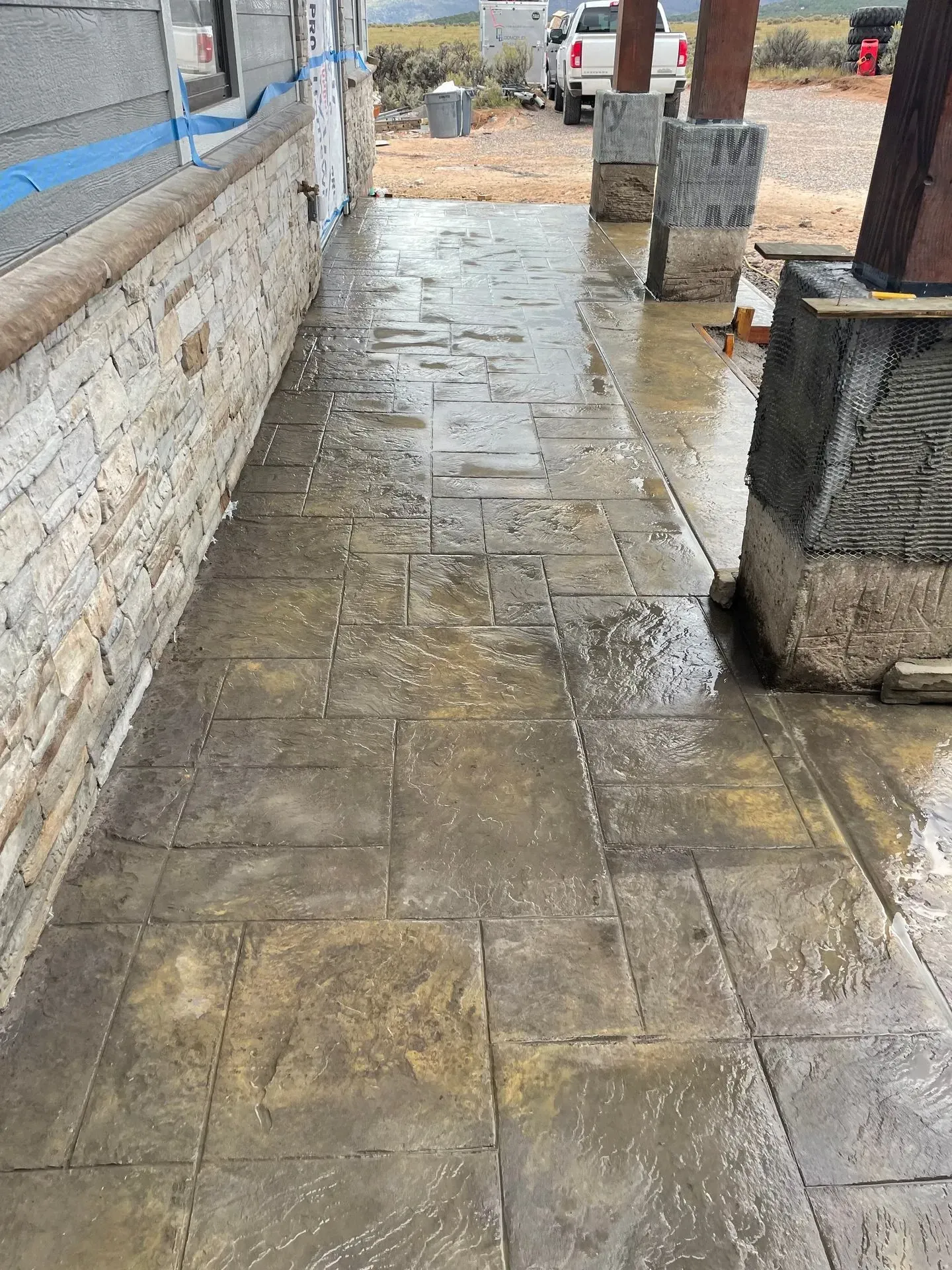 Wet, stamped concrete walkway with a stone wall and support pillars.