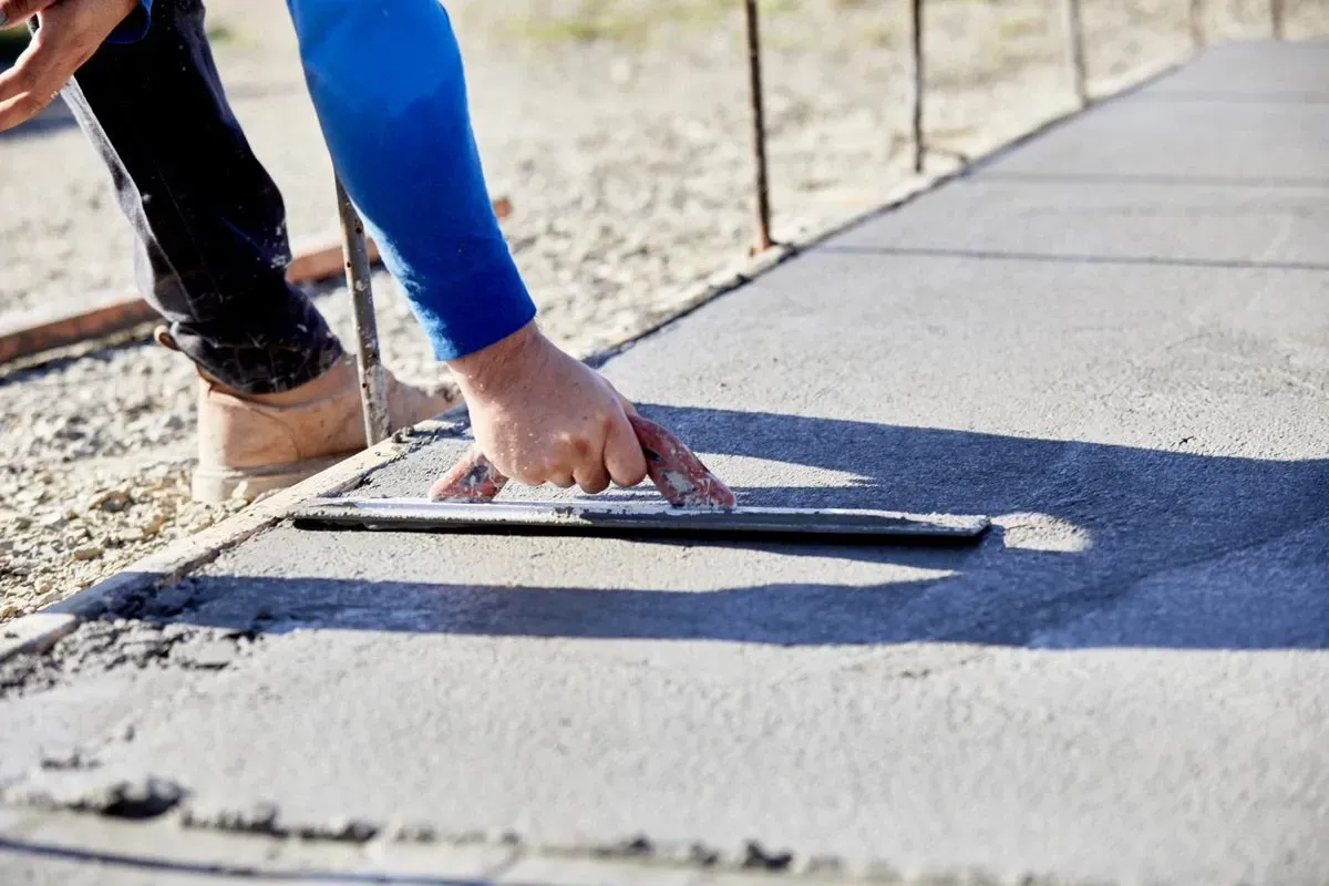 Person smoothing wet concrete sidewalk with a trowel outdoors.