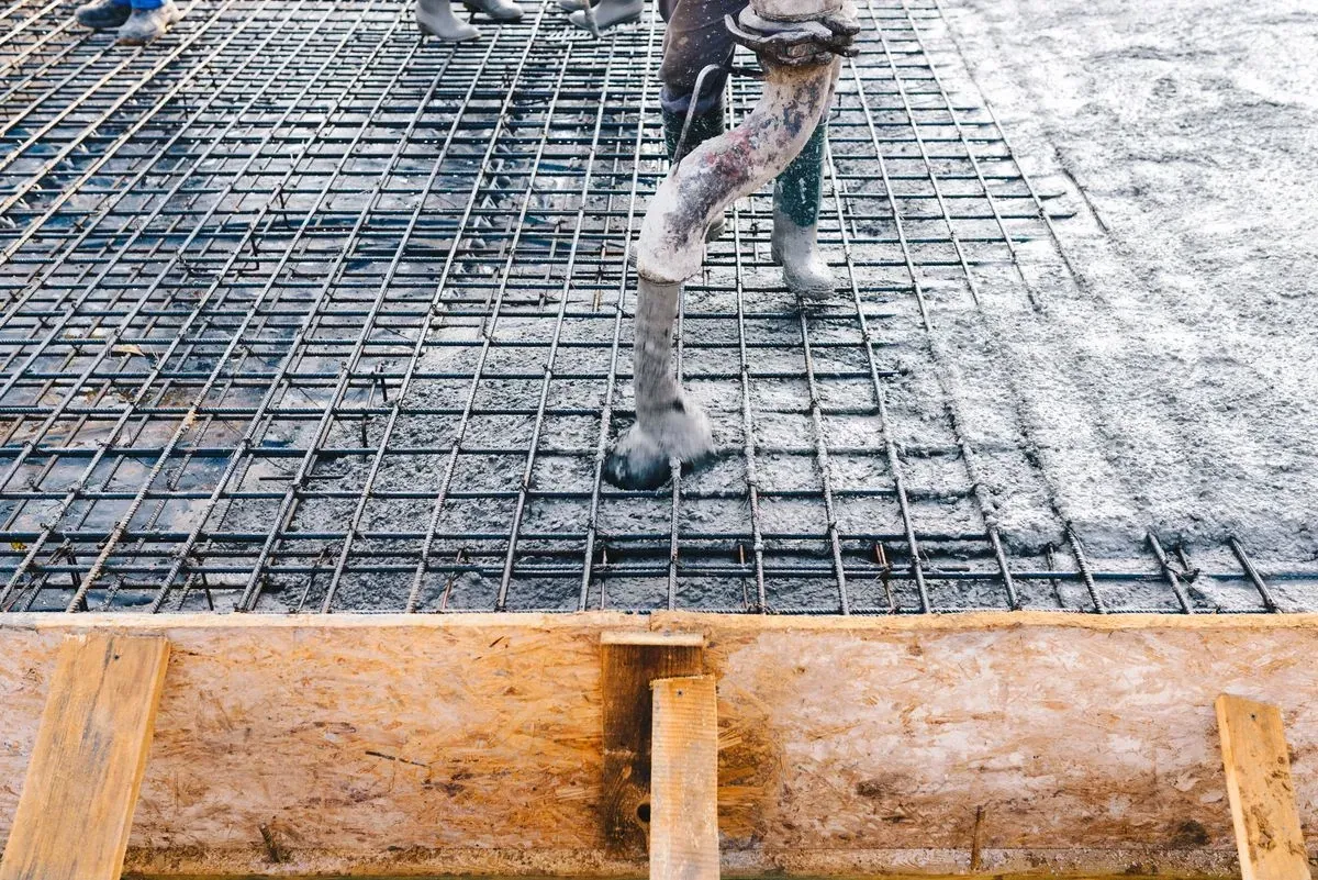Concrete being poured over rebar grid within wooden frame.