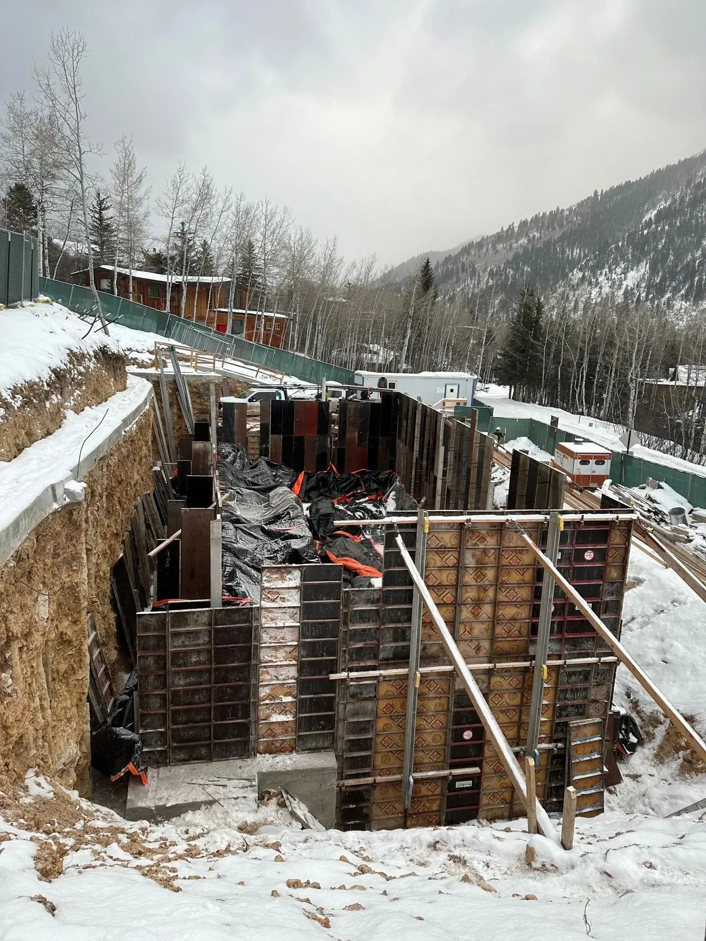 Construction site with wood forms, snow, and a mountain backdrop.