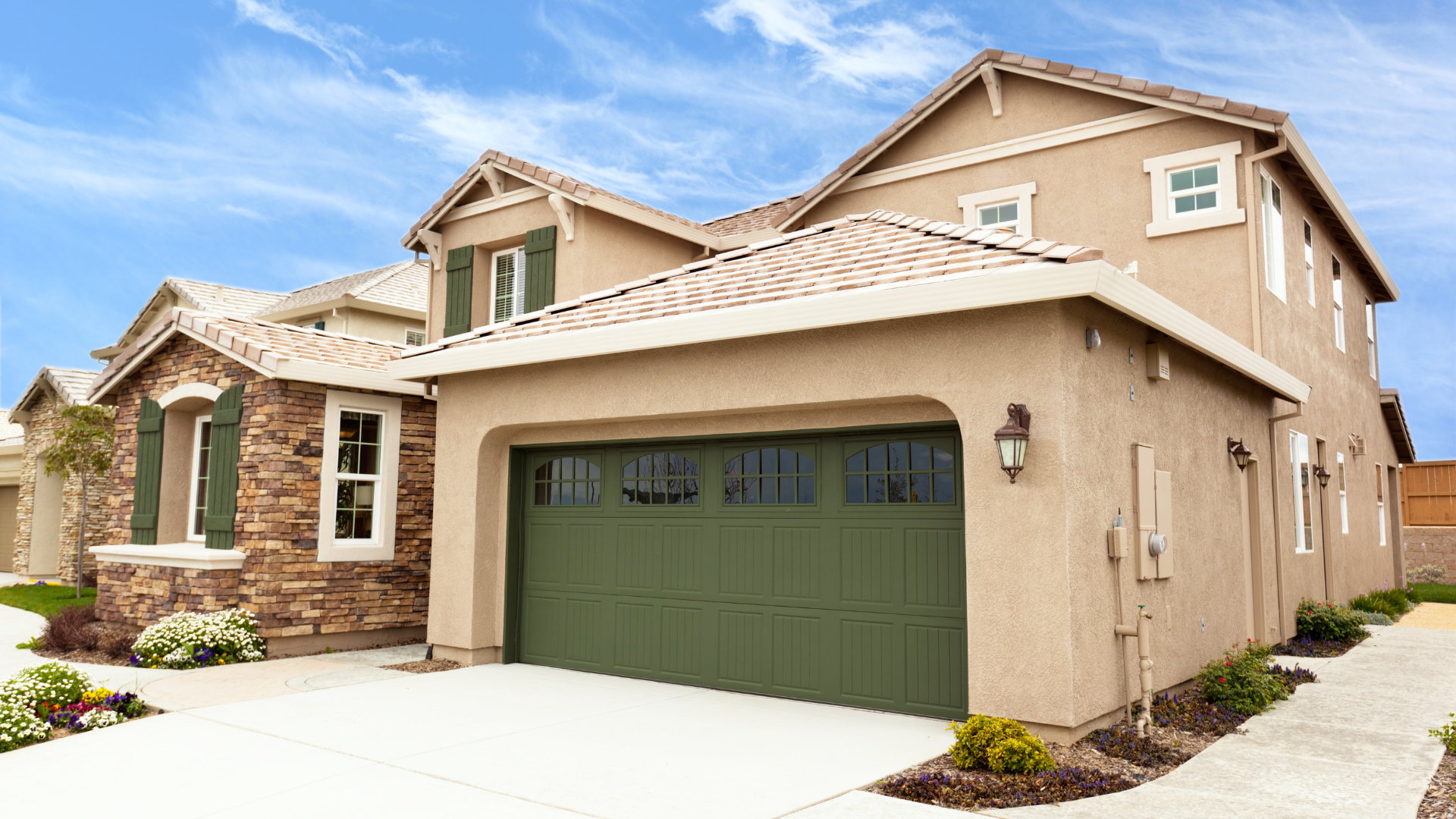 Beige two-story house with green garage door, stone accents, and blue sky.