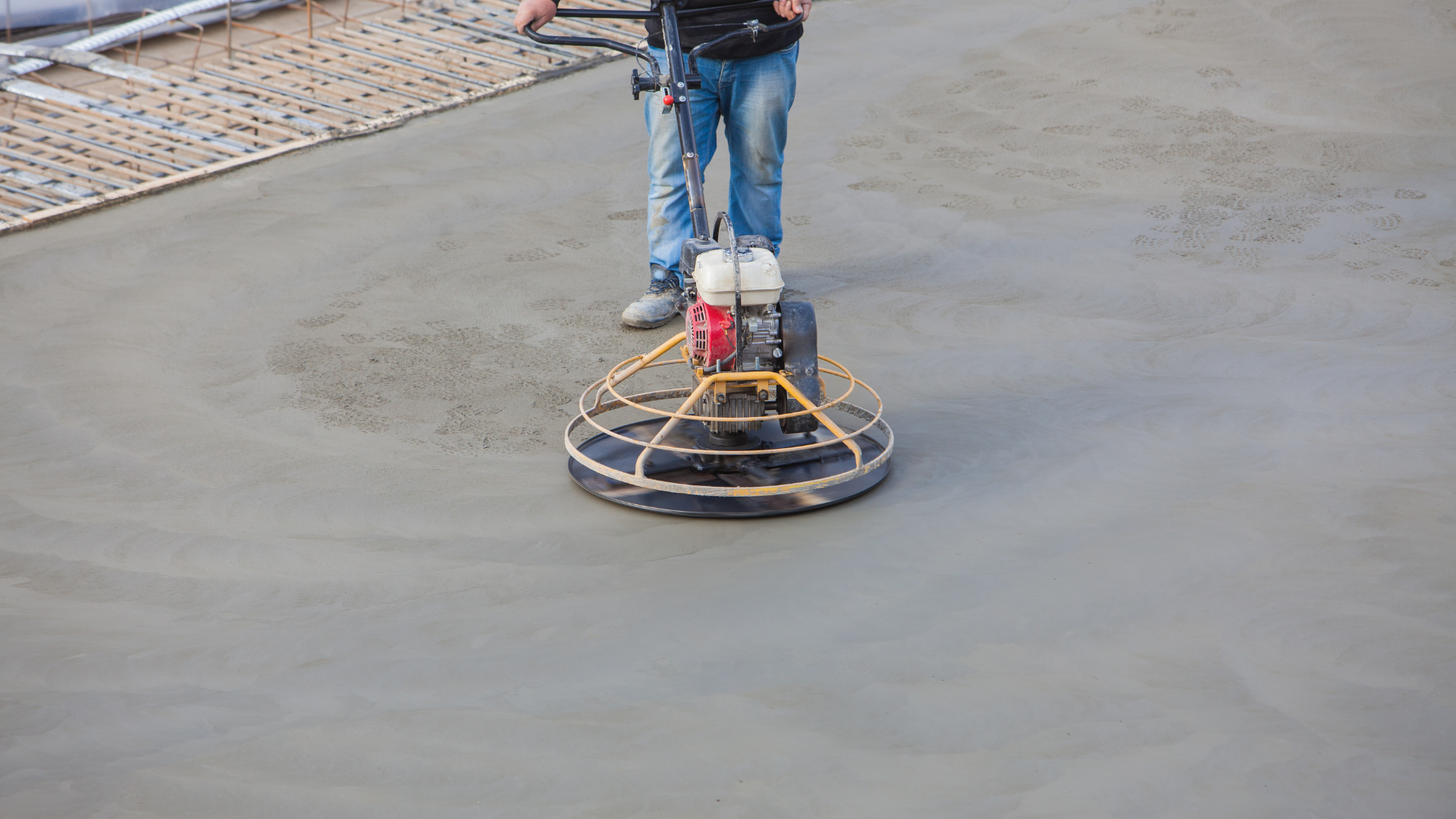 Person operates a power trowel on a concrete surface.