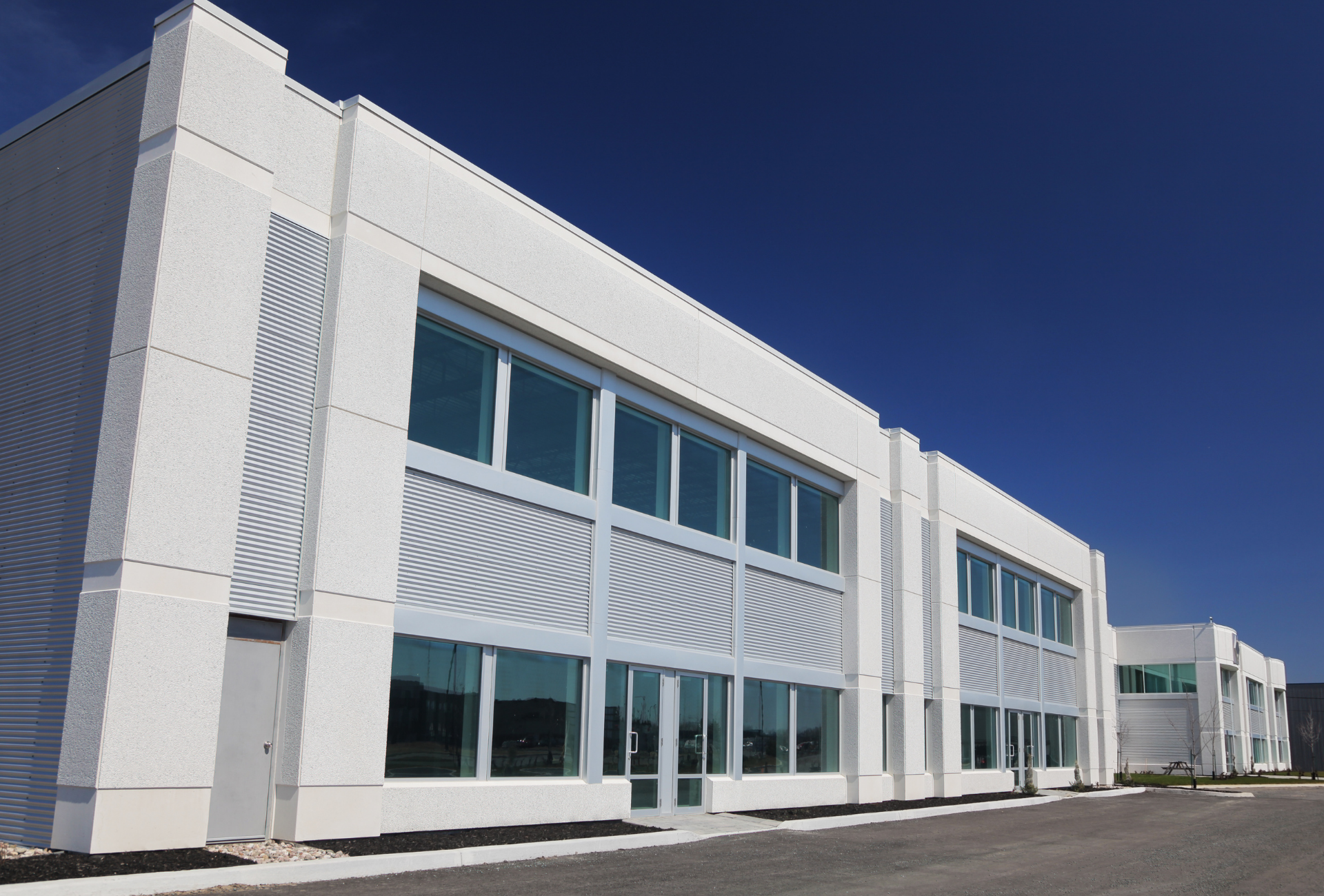 White, modern commercial building with large windows against a clear blue sky.
