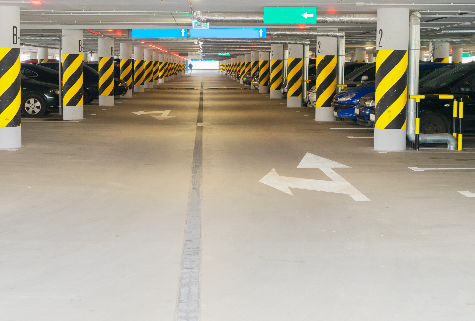 Indoor parking garage, columns with black and yellow stripes, cars parked, directional arrows.