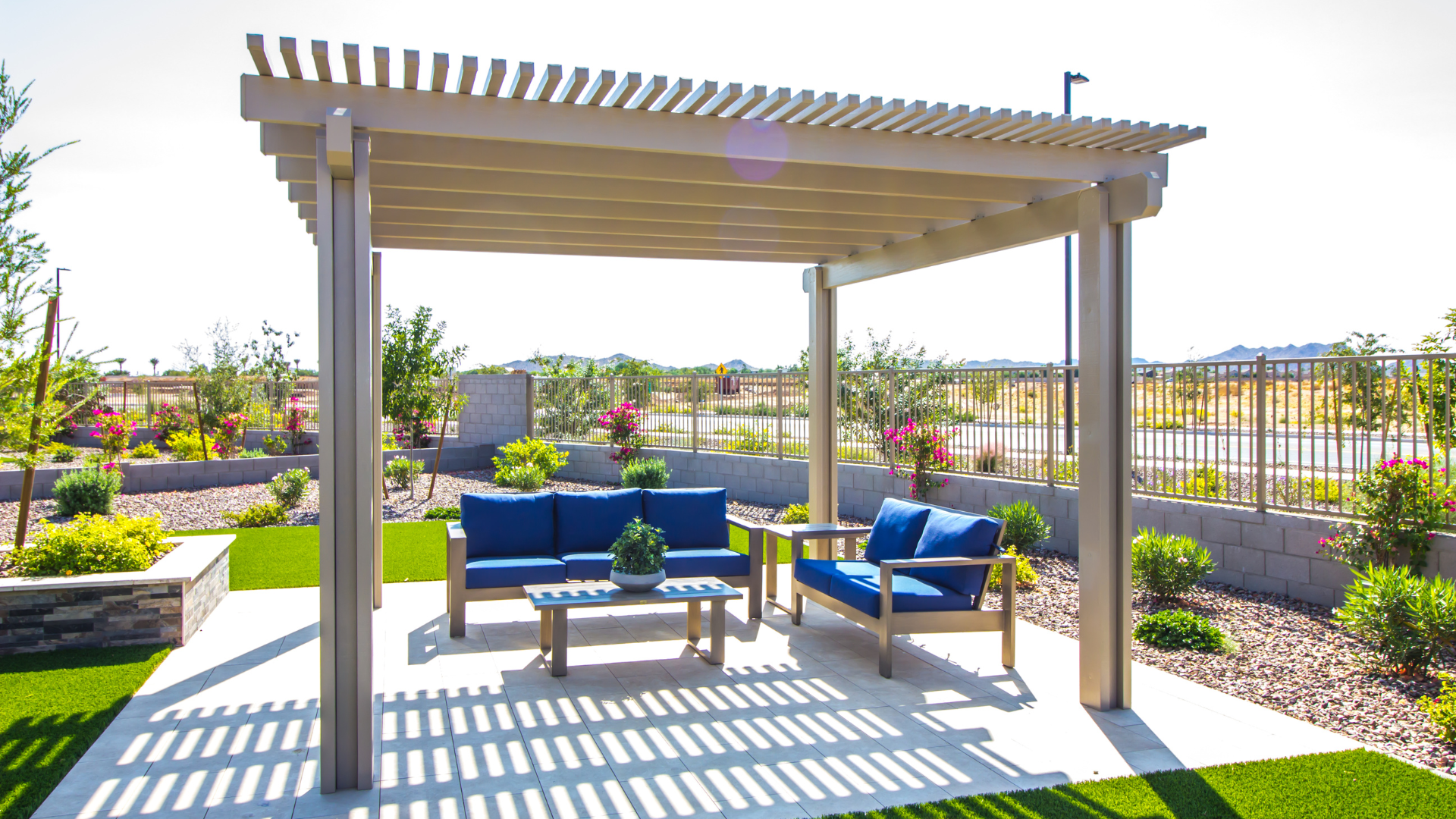 Pergola with blue seating on a concrete patio, surrounded by landscaping.