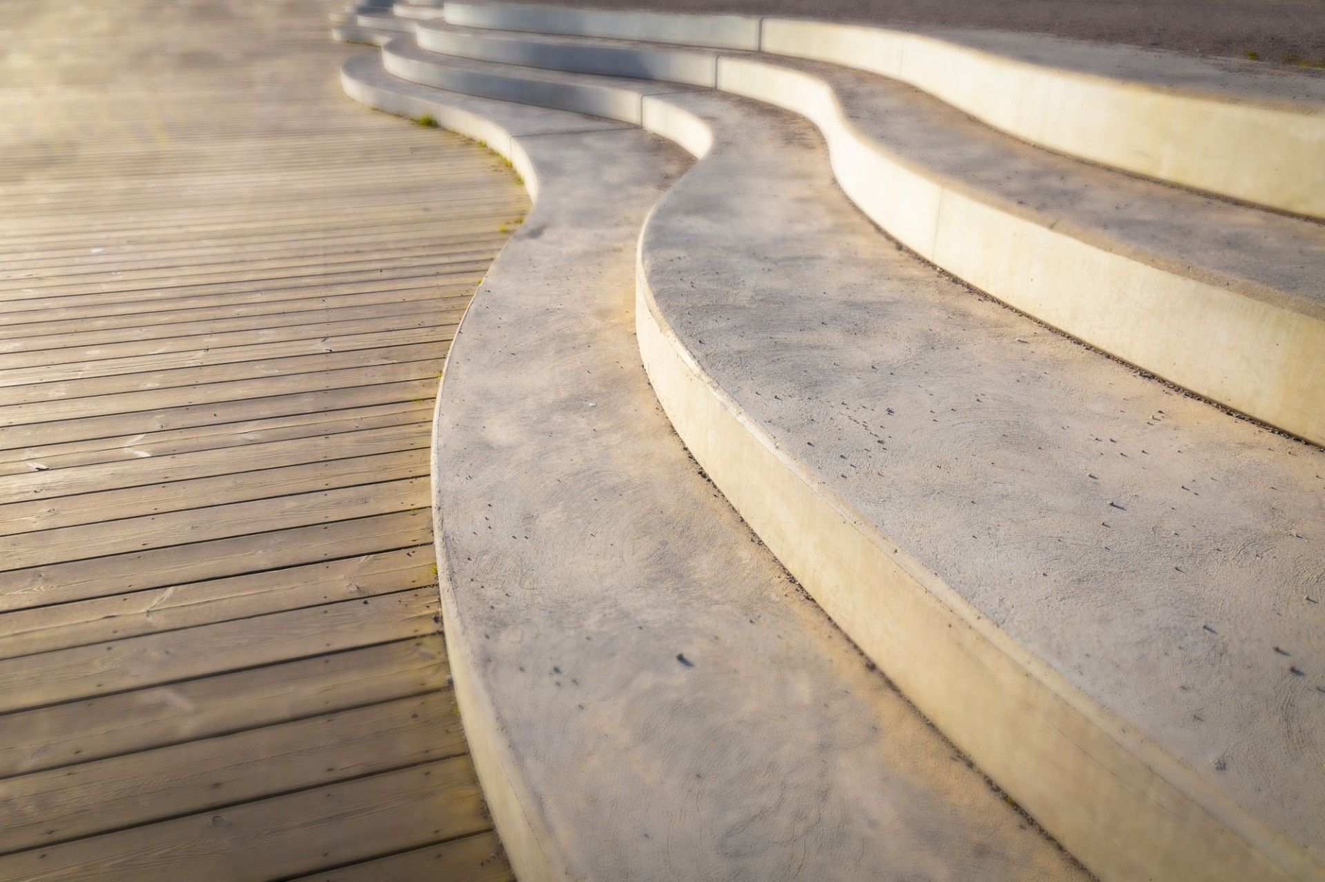 Curved concrete steps leading down to a wooden deck, lit by sunlight.