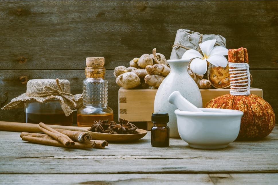 Wooden table with apothecary items: bottles, herbs, mortar and pestle, and a massage ball.