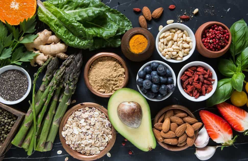 Overhead shot of various healthy foods in bowls, including fruits, vegetables, nuts, and spices.