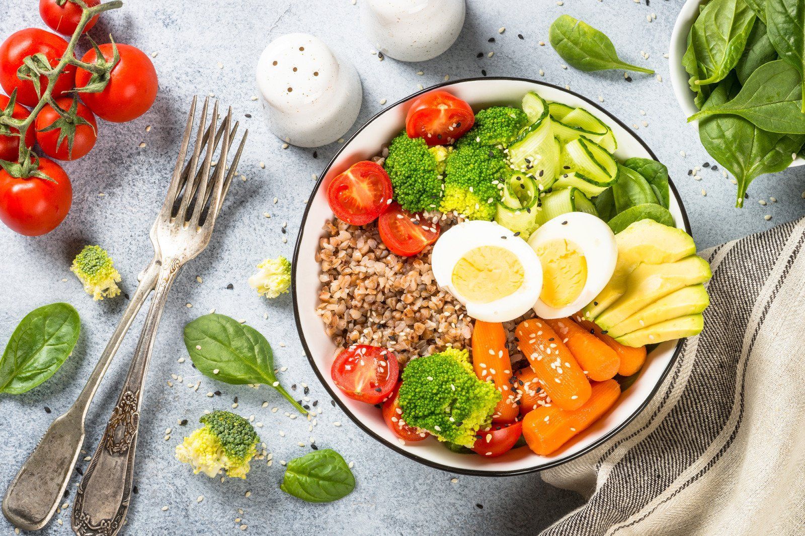 Healthy bowl with vegetables, grains, and egg, with tomatoes and greens on a light-colored surface.