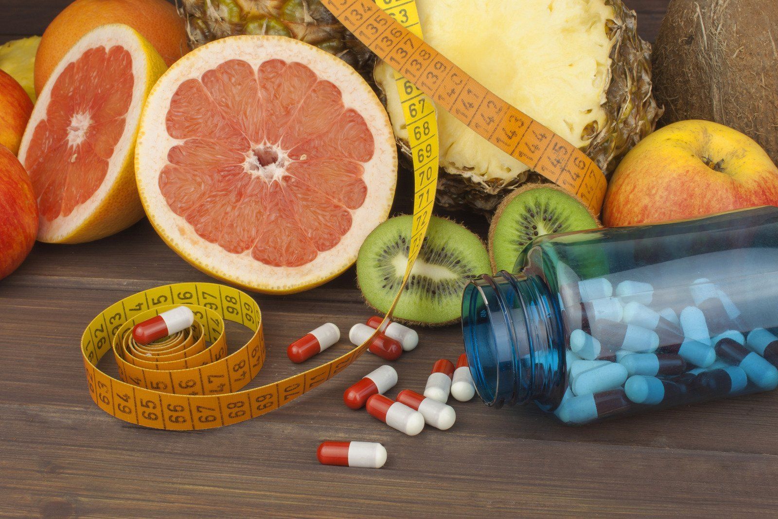 Assorted fruits, pills, and measuring tape suggesting dieting and weight loss on a wooden surface.