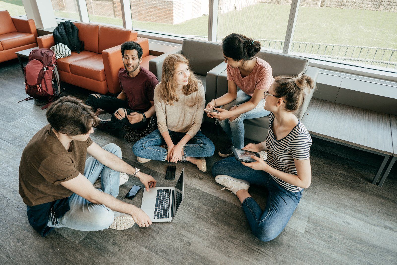 A group of students sitting on the floor in a lounge, collaborating on a laptop.