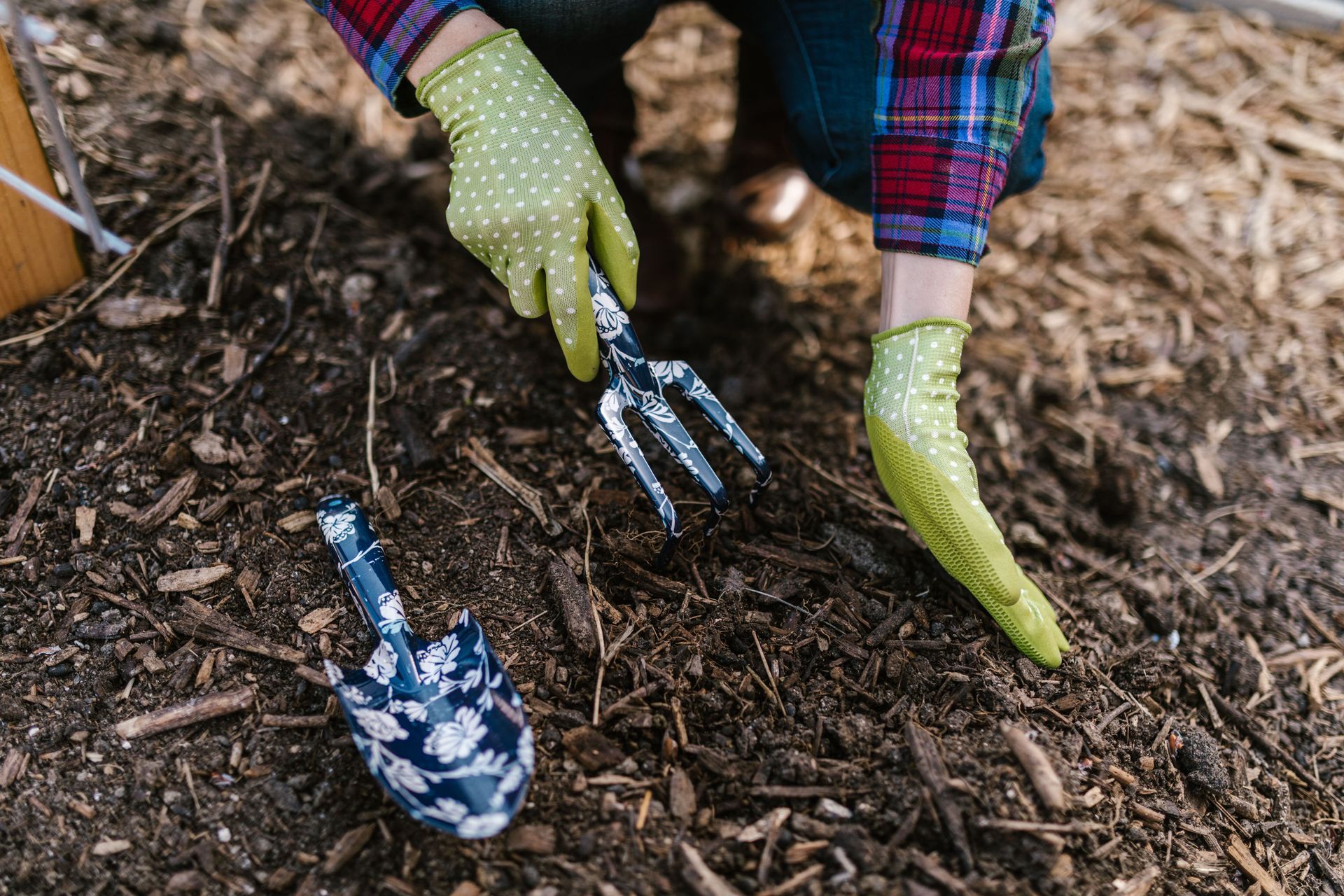Gardening gloves raking mulch with a small hand rake on the ground