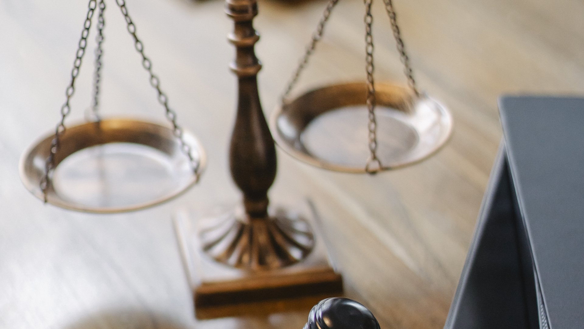 A scale of justice is sitting on a wooden table next to a book.