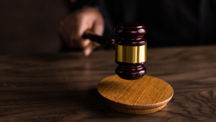 A judge is holding a wooden gavel on a wooden table.