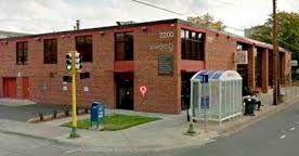 Brick corner building on a street, with a glass bus shelter and blue mailbox on the sidewalk.