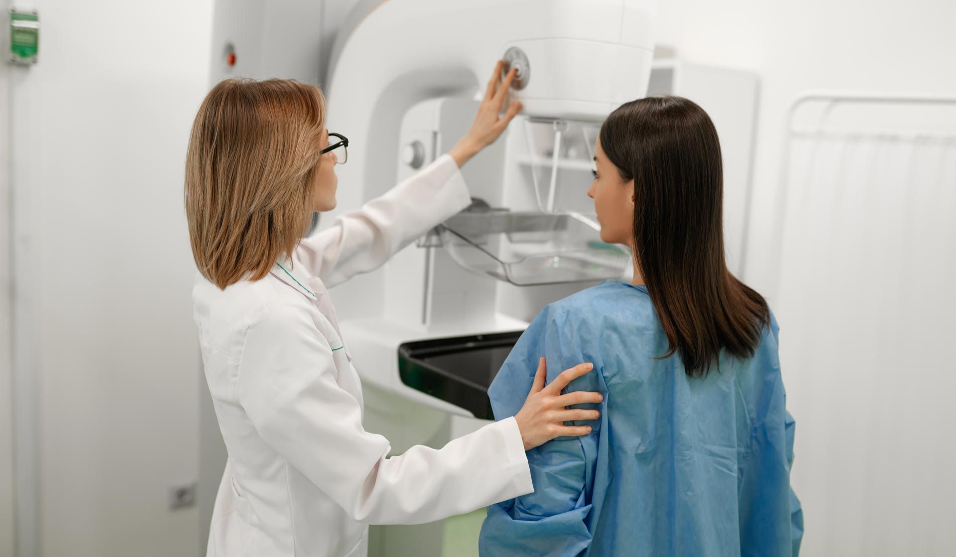 A female doctor assists a patient in a blue gown during a mammogram screening, adjusting the mammography machine in a modern medical facility focused on early detection of breast cancer. A female doctor assists a patient in a blue gown during a mammogram screening, adjusting the mammography machine in a modern medical facility focused on early detection of breast cancer.