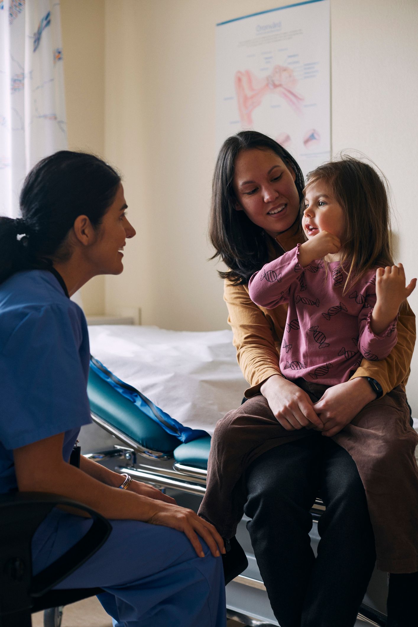 A family doctor is smiling at a woman and her daughter in a hospital room. A family doctor is smiling at a woman and her daughter in a hospital room.