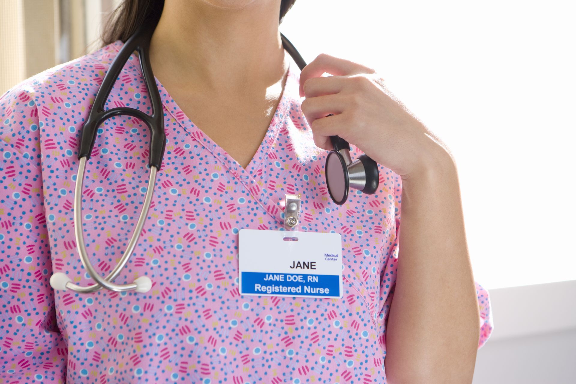 Registered nurse in pink scrubs with stethoscope and ID badge, representing healthcare profession.