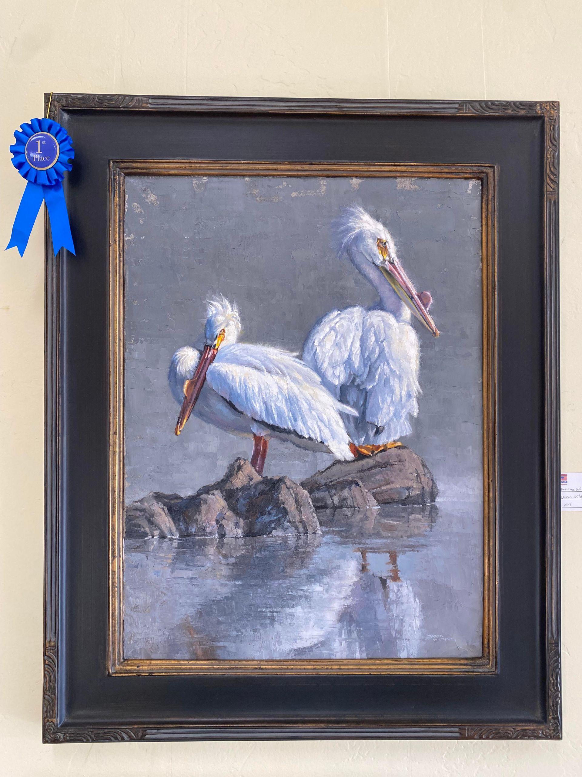 A framed painting of two pelicans with a blue ribbon