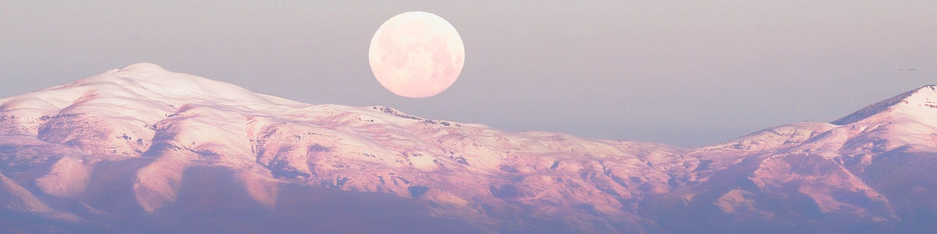 A full moon is rising over a snowy mountain range.