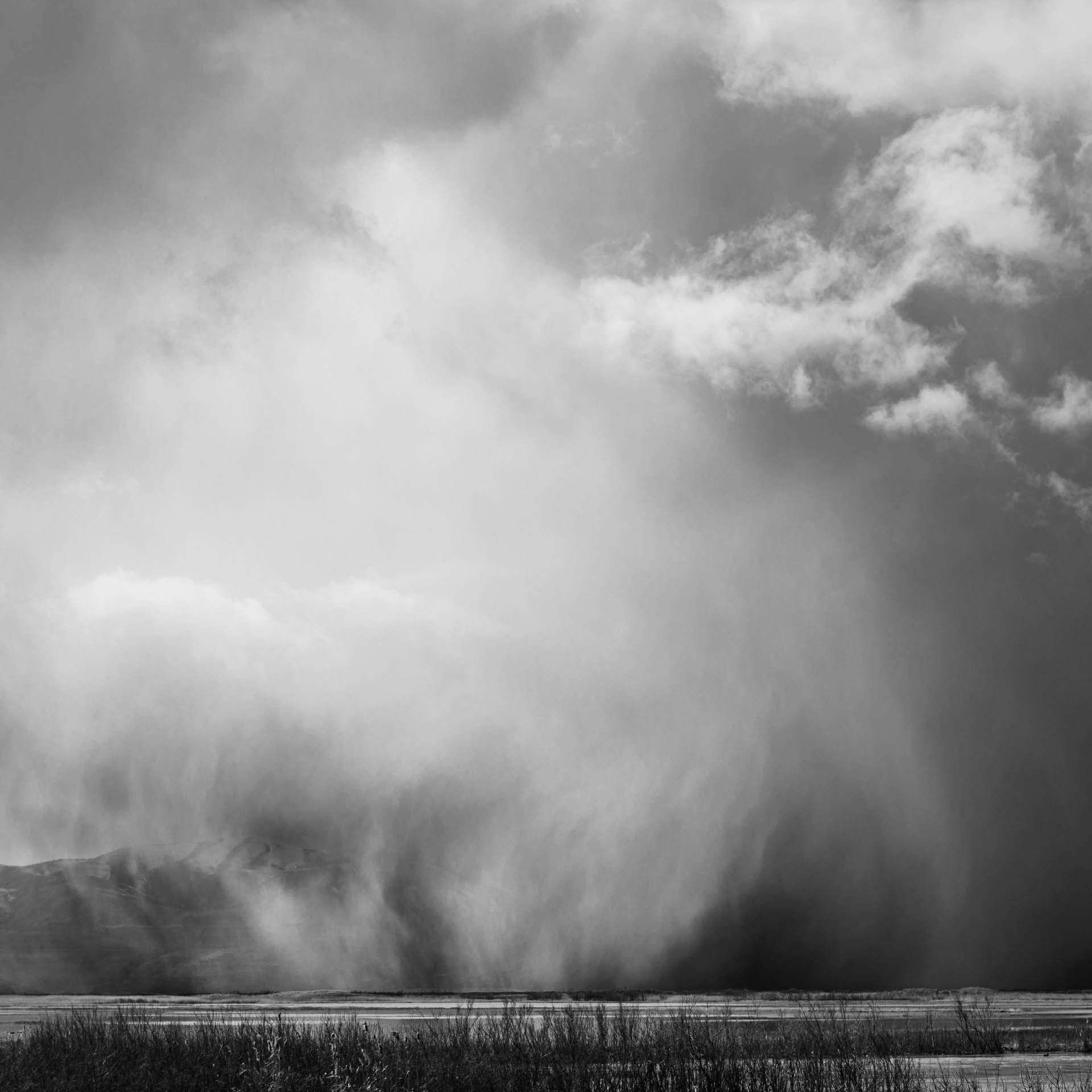 A black and white photo of a cloudy sky over a field.