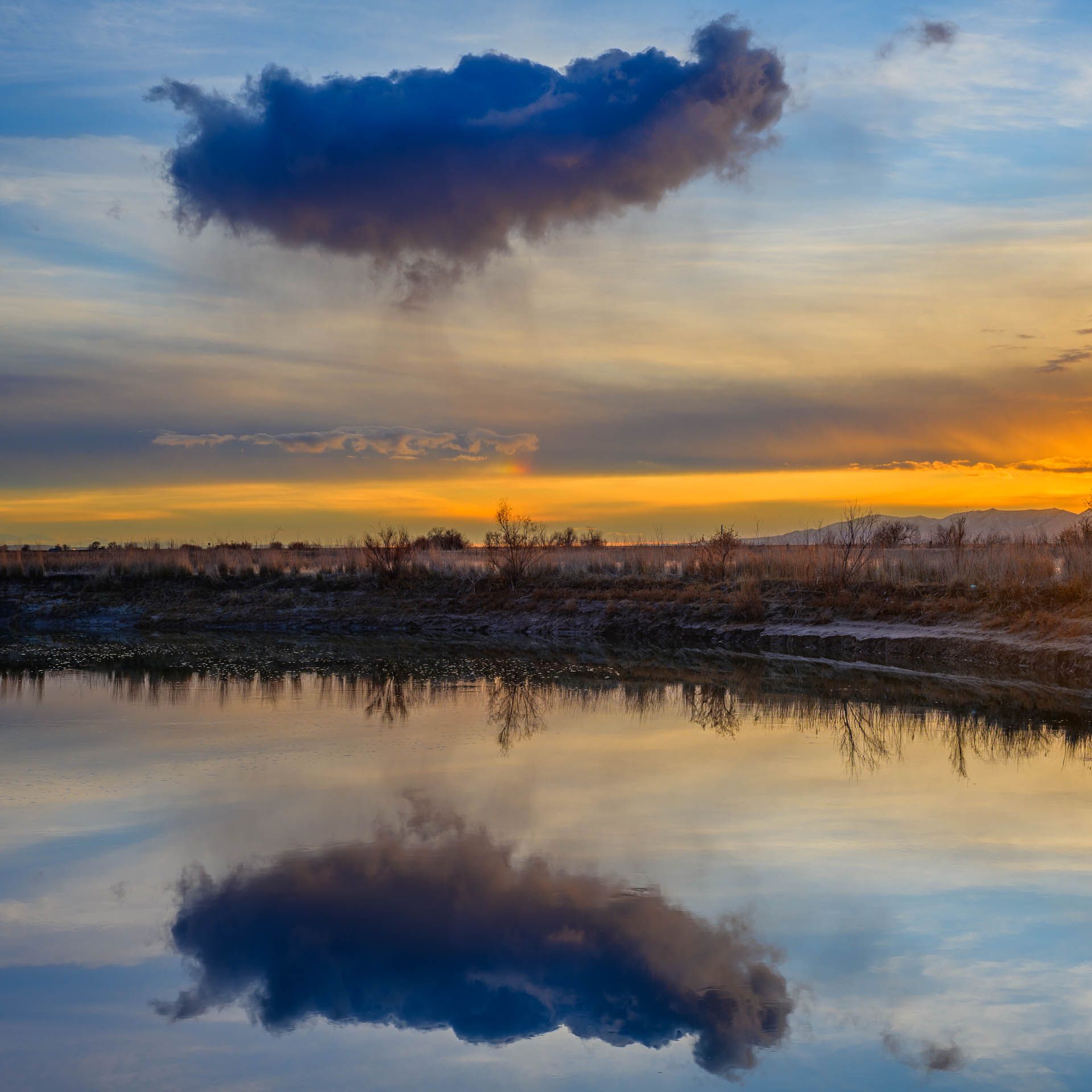 A sunset over a lake with clouds reflected in the water.