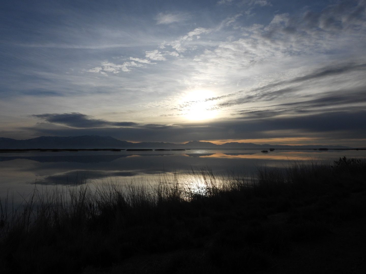The sun is setting over a lake with mountains in the background