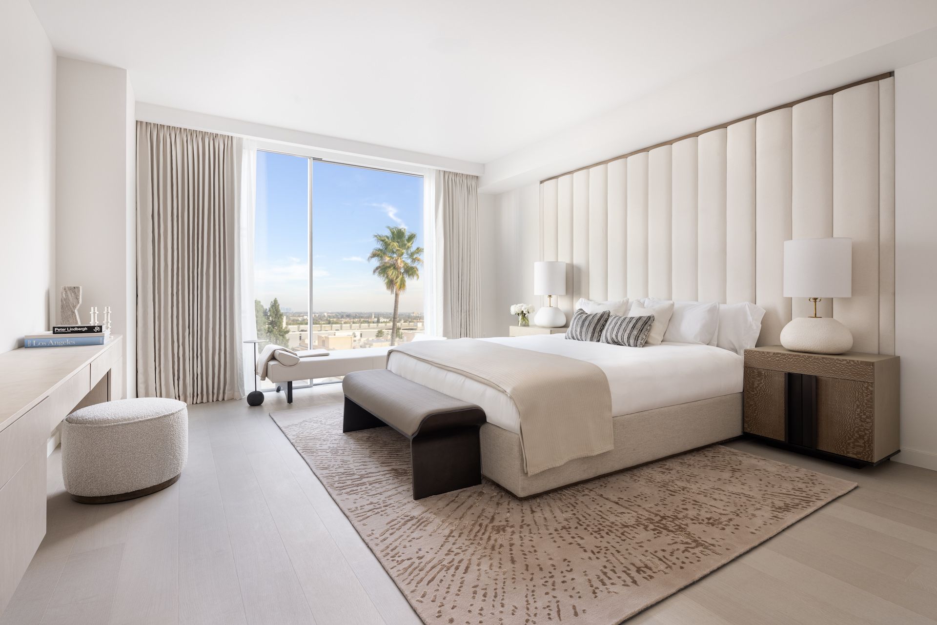 A bedroom with a large bed , a bench , and a large window.