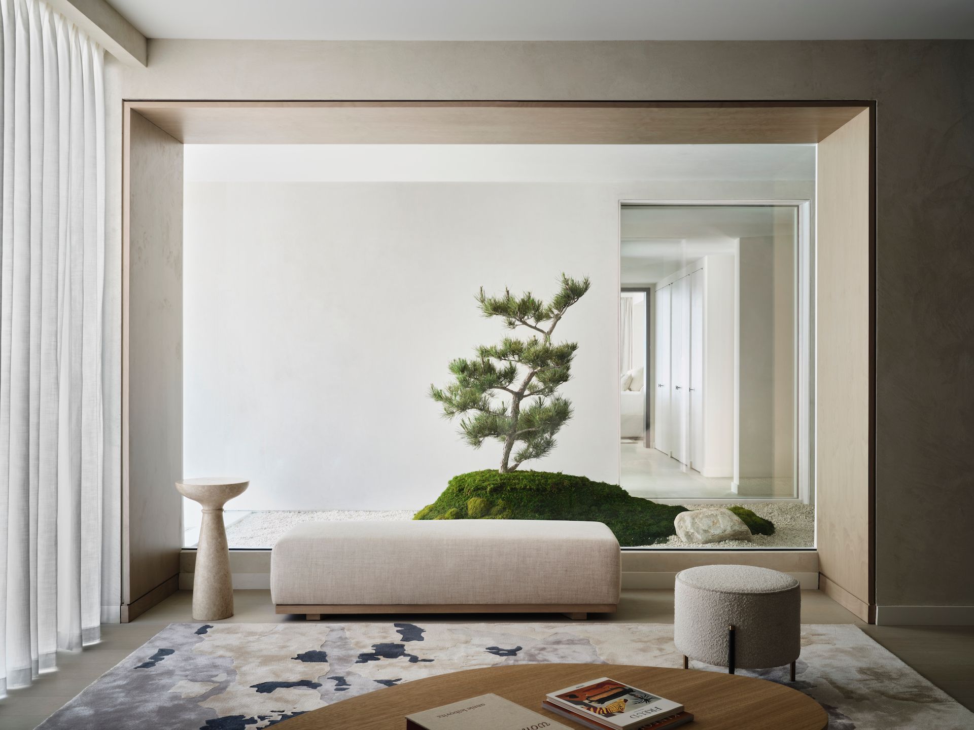 A living room with a bench , ottoman , coffee table and a tree in the middle.