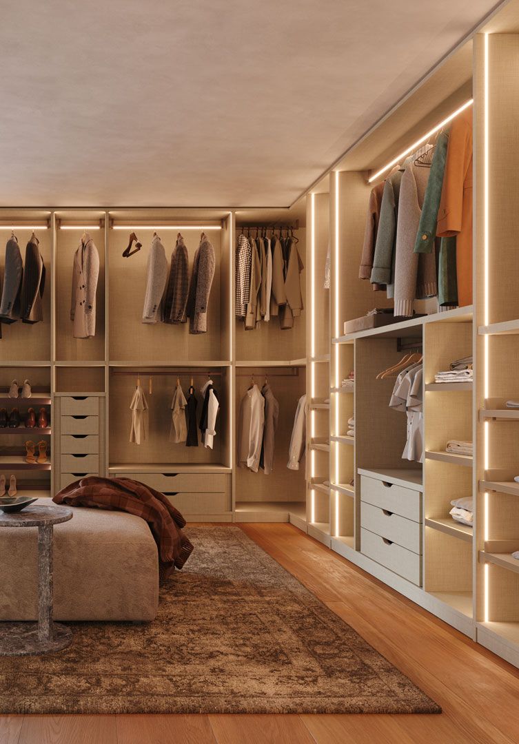 Cabina armadio con mobili beige a muro, luci soffuse e appendiabiti. Include una panca e un tappeto a fantasia.