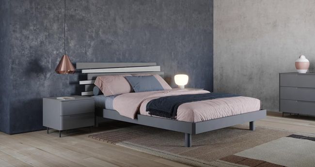 Camera da letto con struttura del letto, comodino, cassettiera e parete grigi, con biancheria da letto rosa e blu.