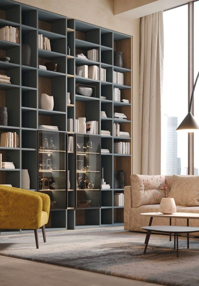 Soggiorno con una grande libreria a muro, una poltrona gialla e un divano beige, con una grande finestra.