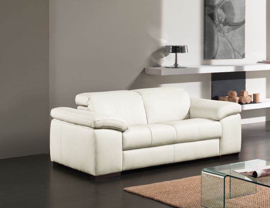 Divano in pelle color crema in un soggiorno moderno. Una piccola lampada e quadri astratti decorano la parete.