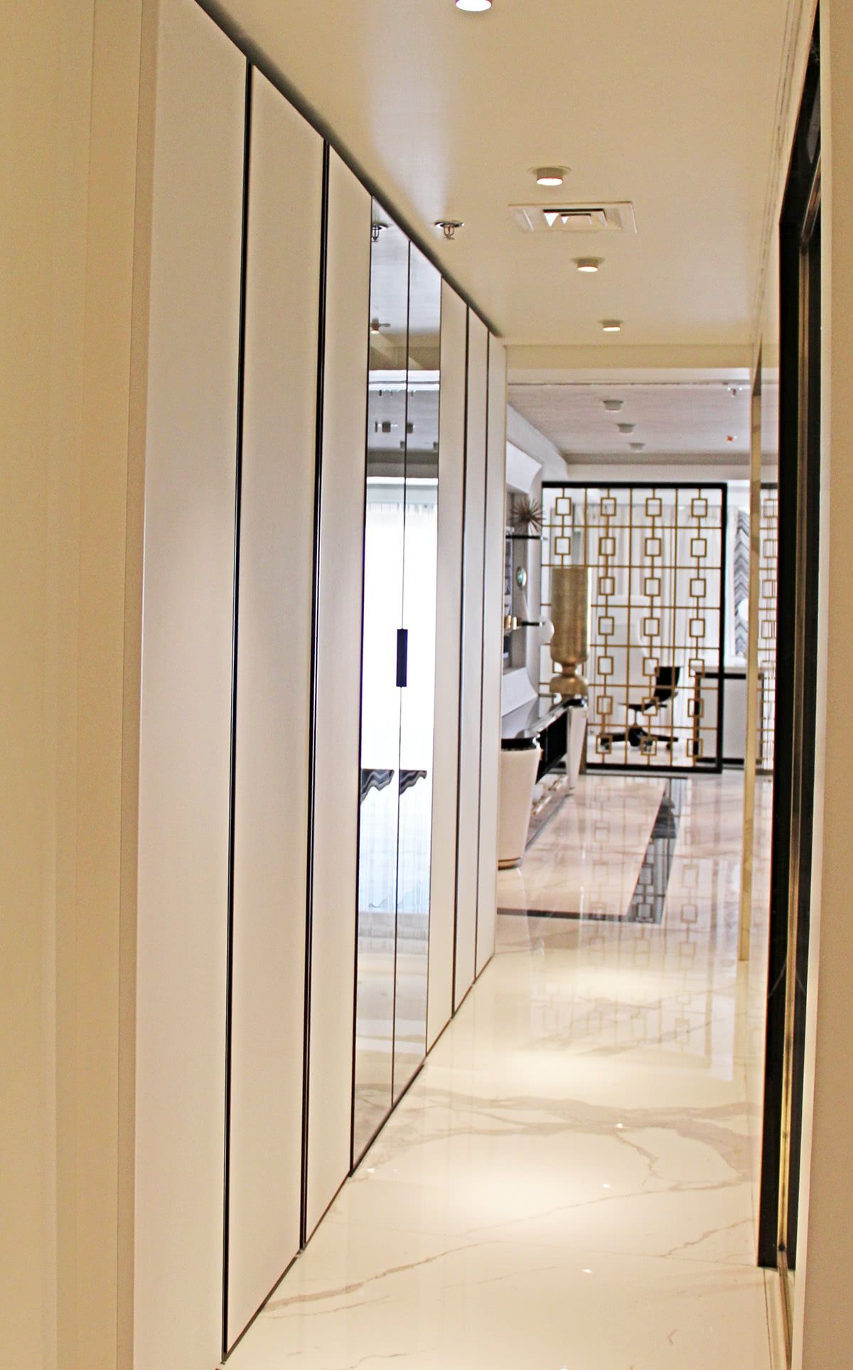 Corridoio stretto con pareti rivestite di pannelli bianchi, un armadio a specchio e pavimento in marmo.