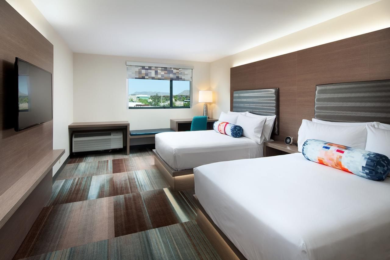 Camera d'albergo con due letti, TV e finestra. Dettagli marroni e blu in tutto l'ambiente.